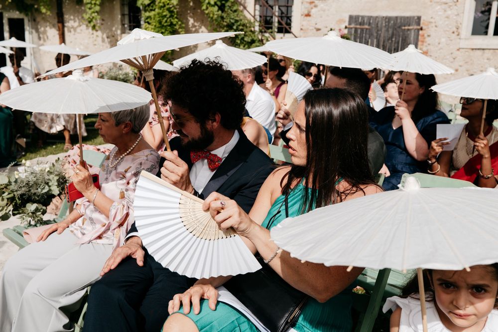 Wedding attendees gathered outside with white paper parasols creating a festive summer atmosphere.