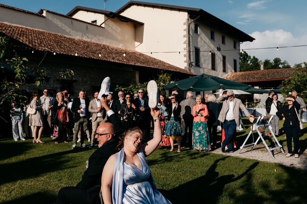 Wedding guests gather outdoors on a sunny day near a rustic white building with terracotta roof tiles.