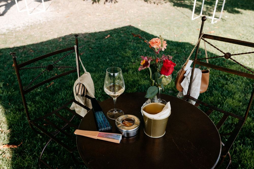 A rustic outdoor dining setup with wine glasses and table settings under a garden pergola.