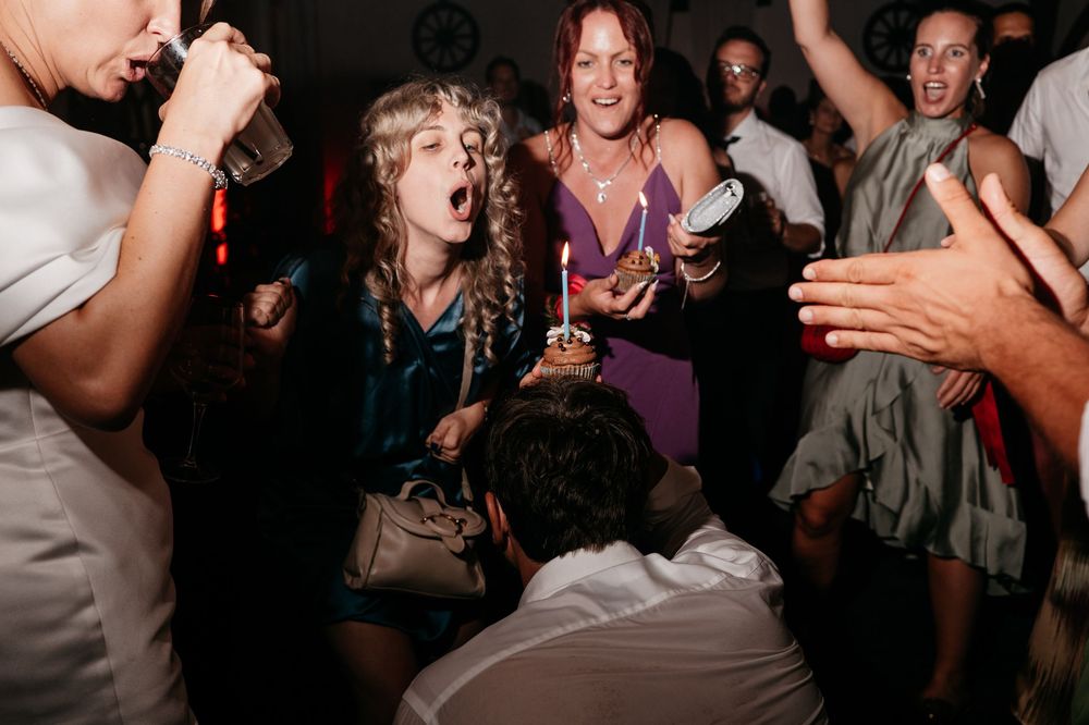 People dancing and celebrating energetically at a dark nightclub or party with drinks in hand.