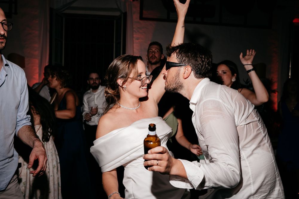 Wedding party dances together in a dark reception venue with string lights creating a festive atmosphere.
