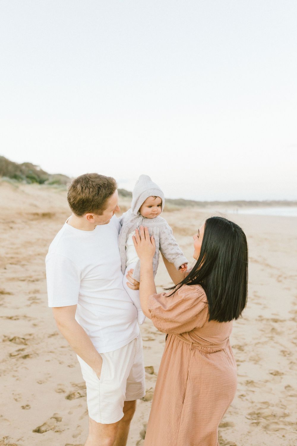 Family in white and peach outfits walking together on a sandy beach during sunset.