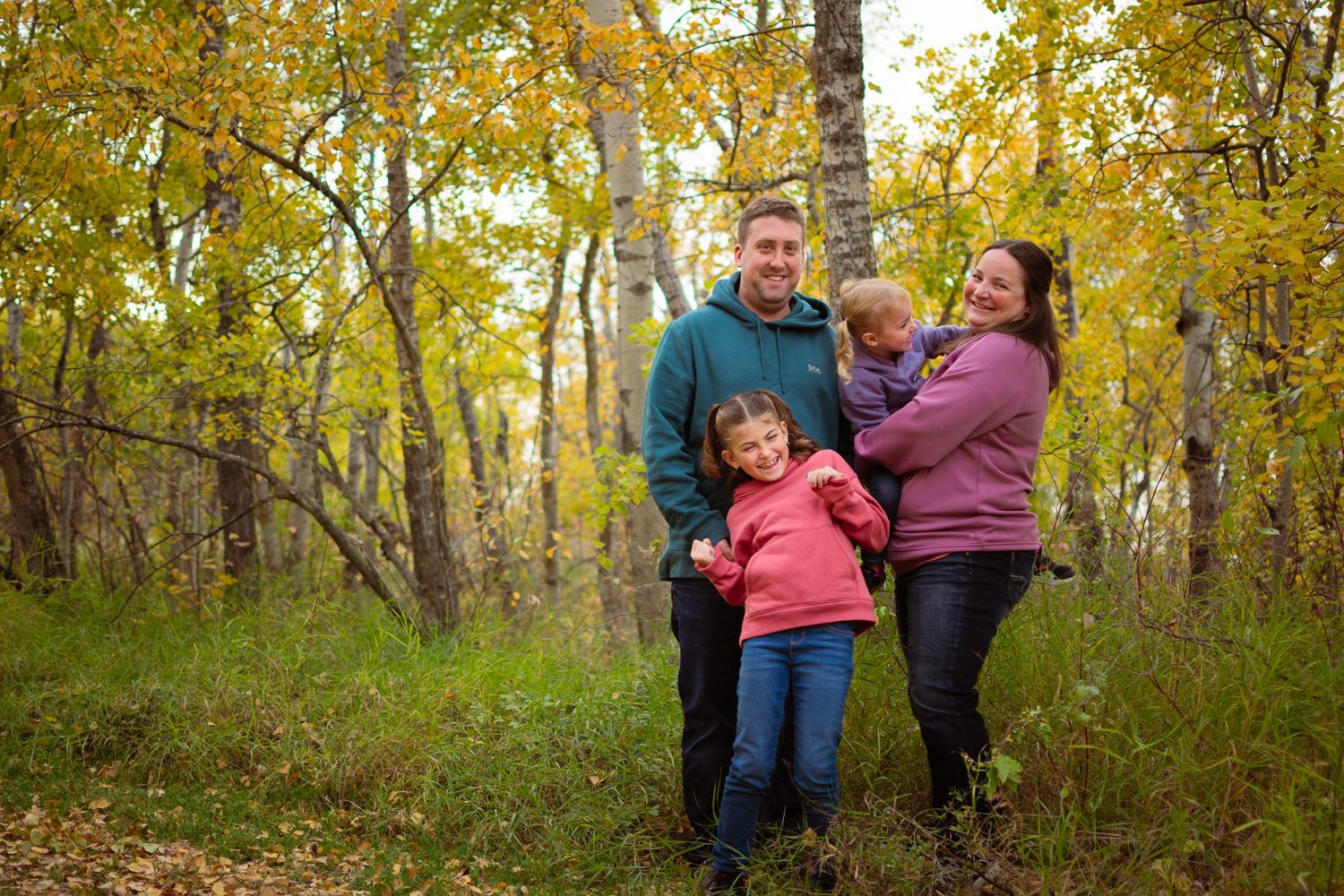 Family shares warm embrace while standing among autumn birch trees.