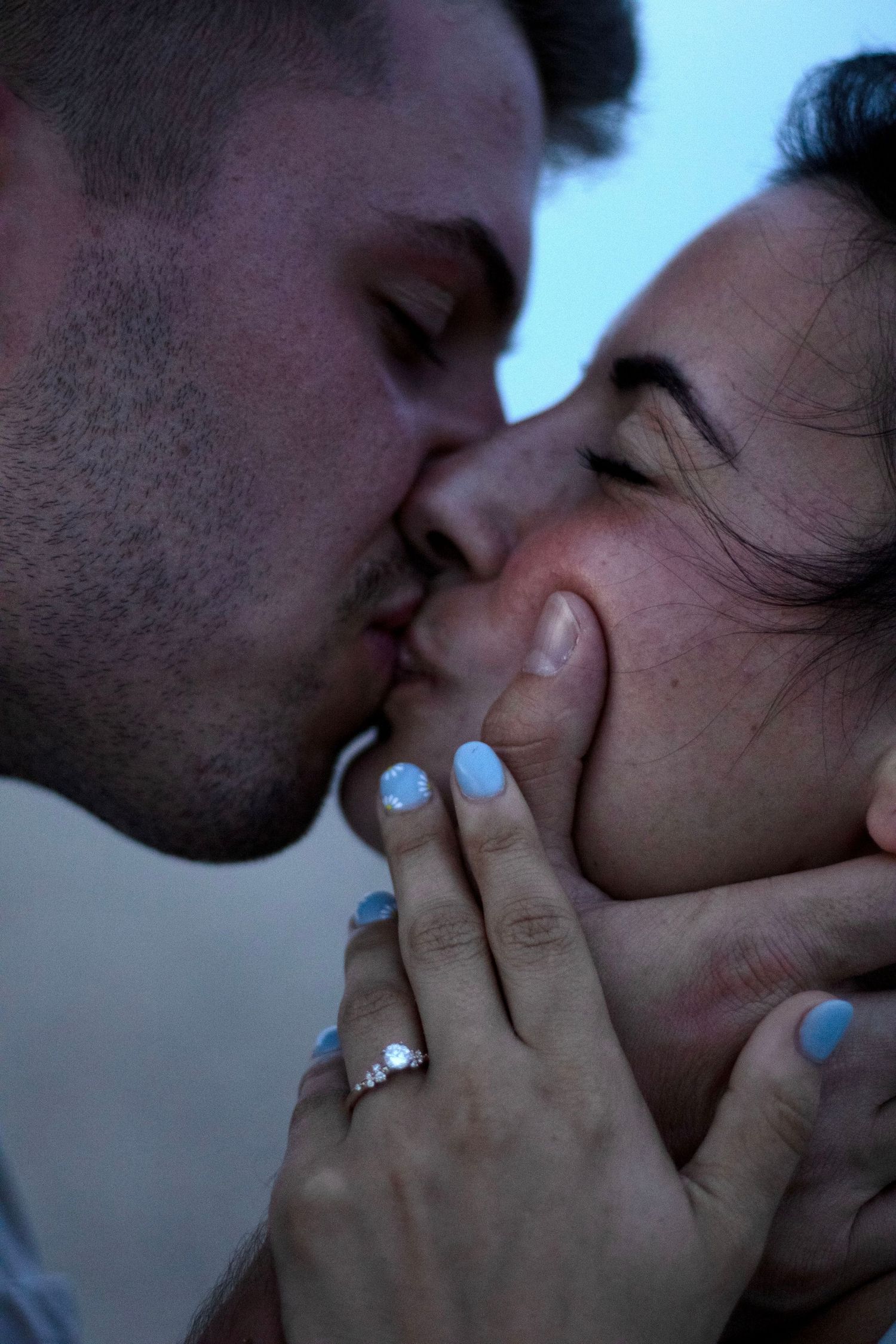 Intimate close-up photo of a romantic kiss with light blue nail polish visible on displayed hands.