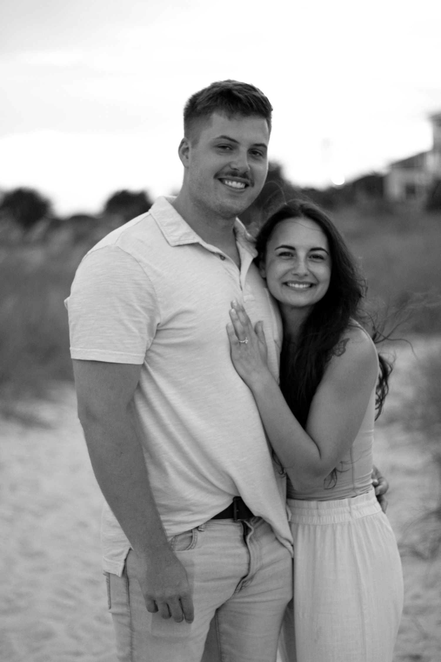 Couple in white outfits embracing on a beach in black and white photos.