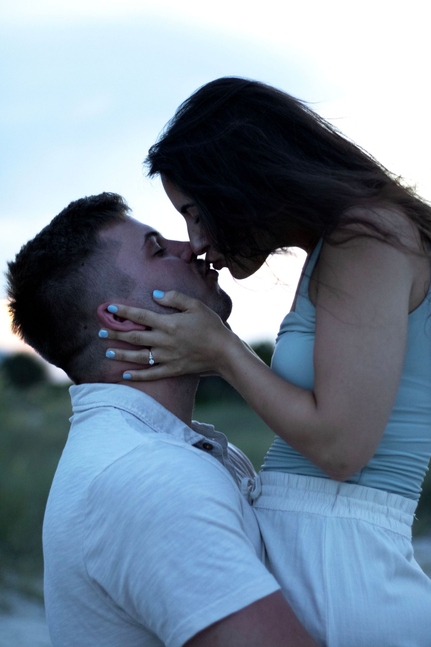 Romantic sunset photo of an intimate moment between a couple with an engagement ring visible.