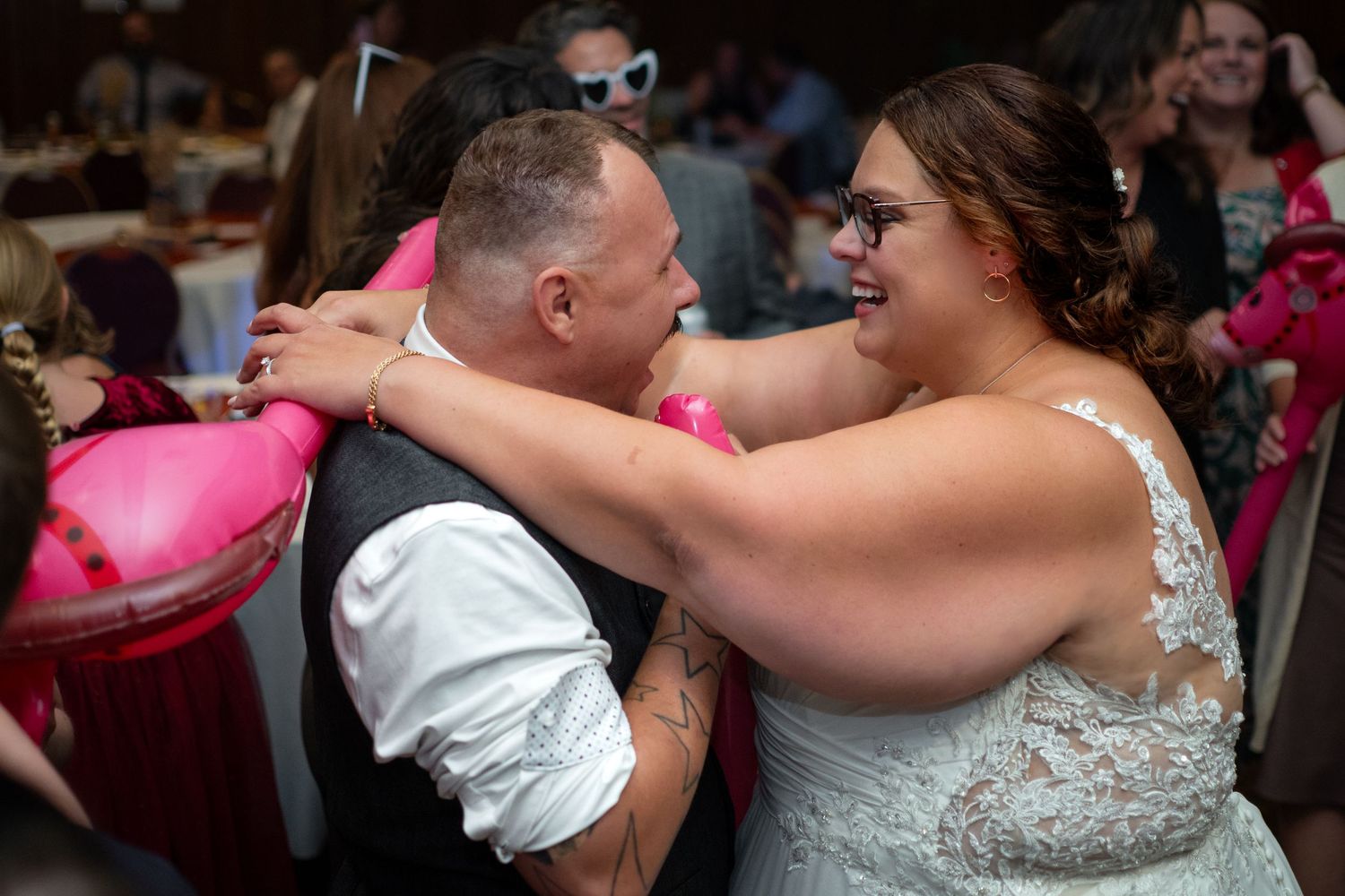 Dancing couple celebrates joyfully at wedding reception with pink decor.