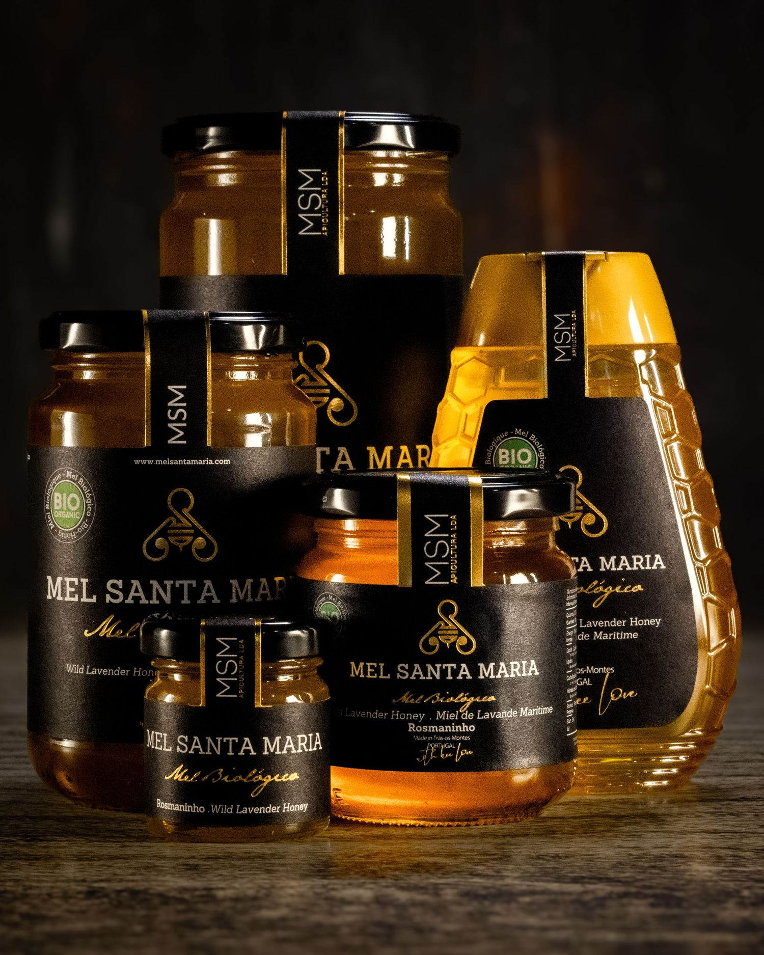 Collection of illuminated honey jars with Santa Maria branding displayed on dark surface.