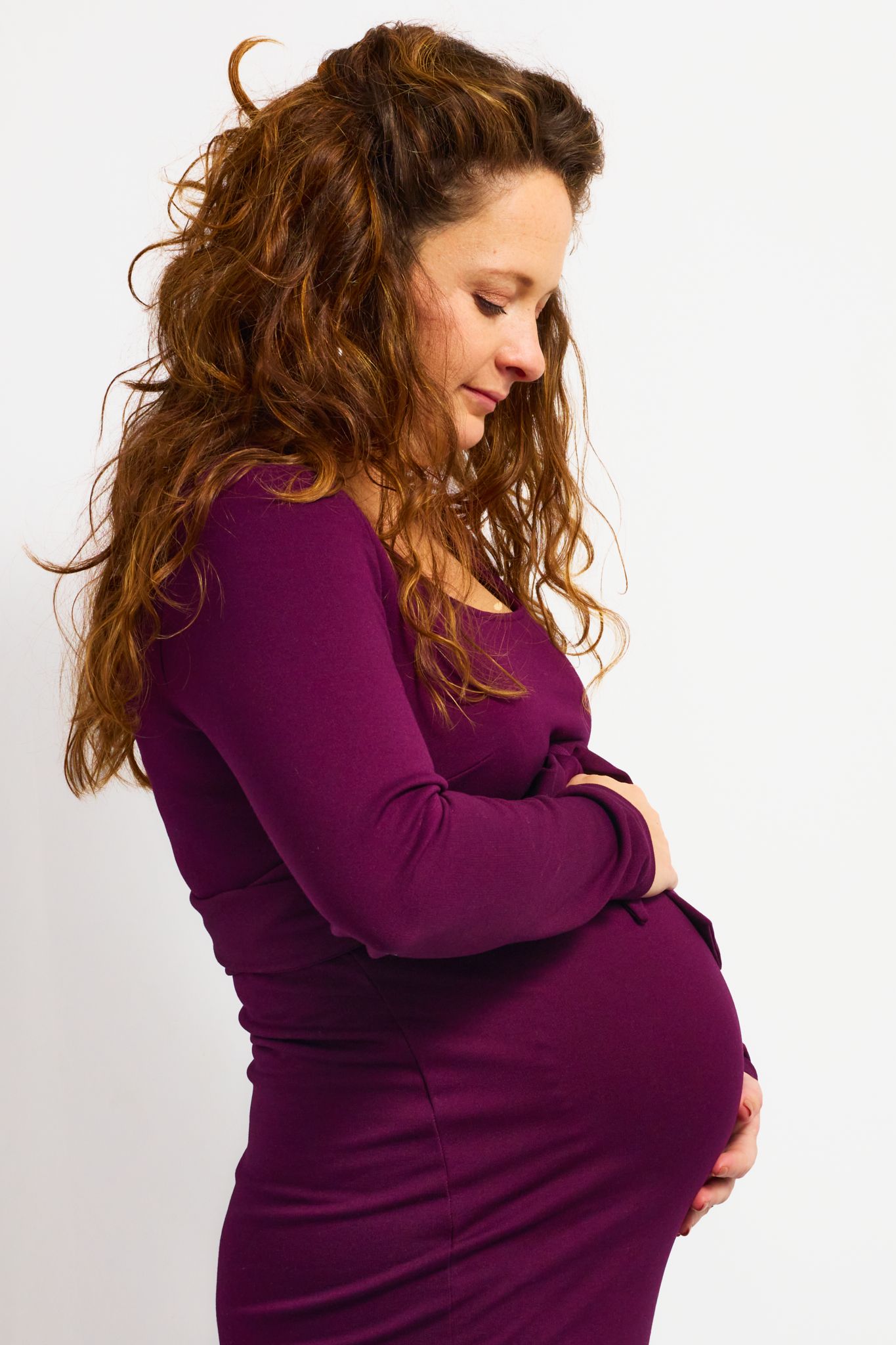 Maternity portrait series showing woman in purple sweater cradling baby bump.