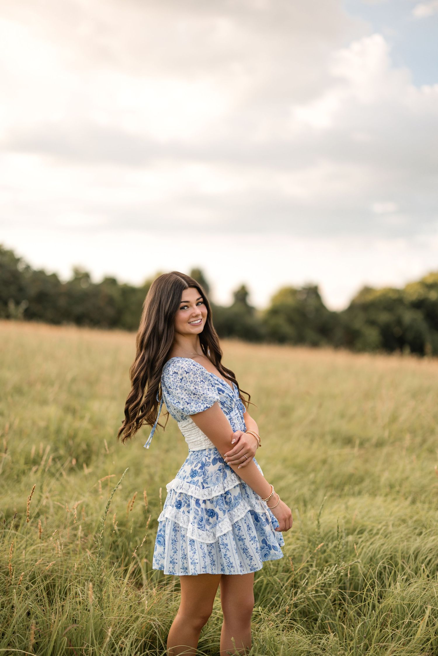 Young girl in blue floral dress spins and dances playfully in a golden summer meadow at sunset.