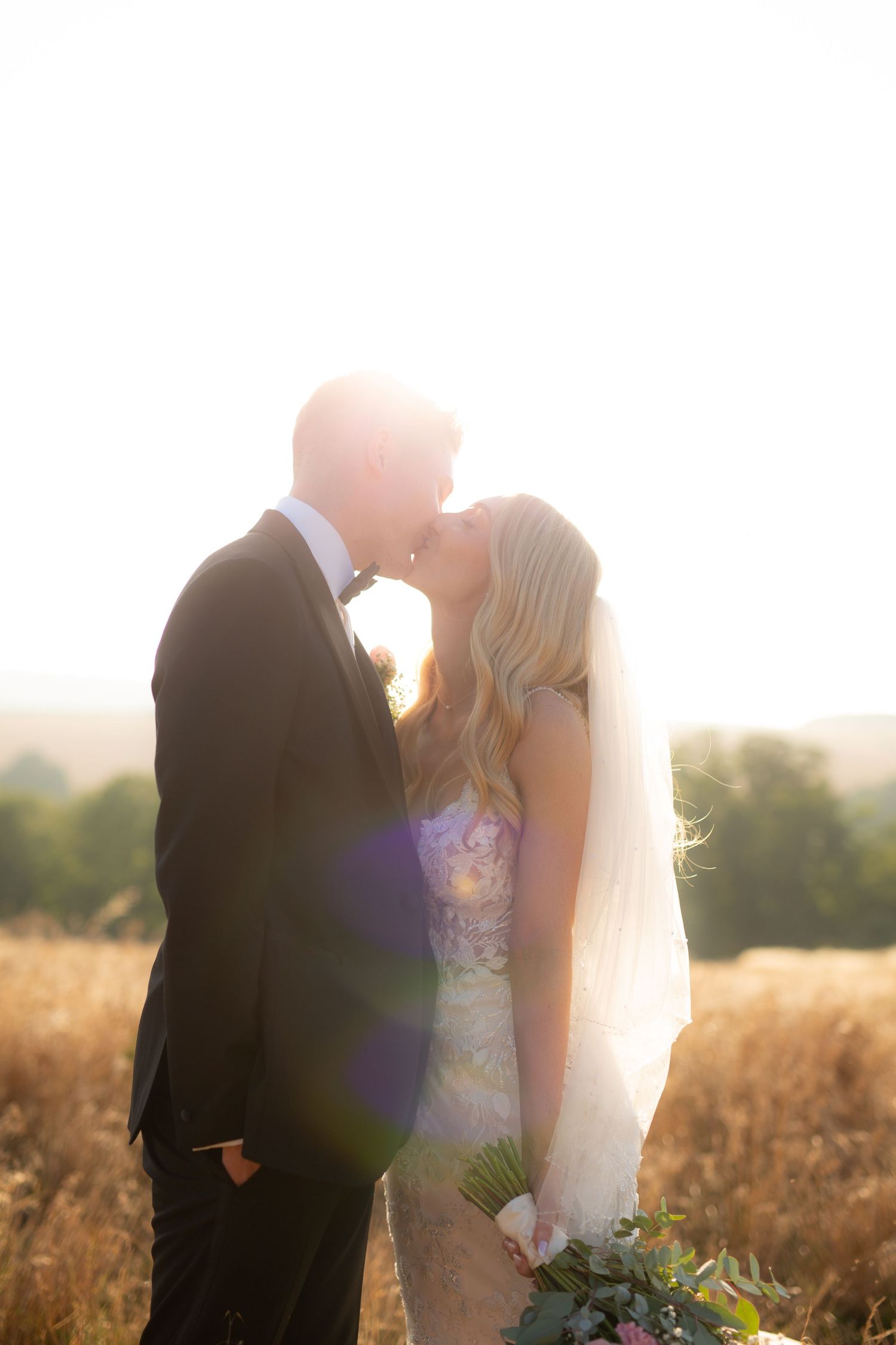 A couple in wedding attire sips drinks together under elegant chandeliers at an indoor reception venue.