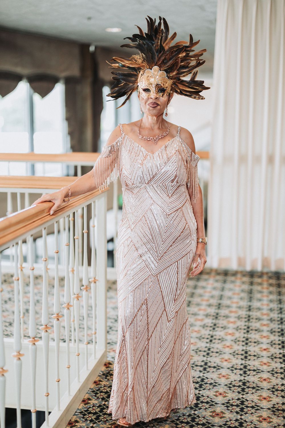 Elegant beaded blush gown with geometric patterns photographed in a luxurious venue with patterned carpet and white curtains.