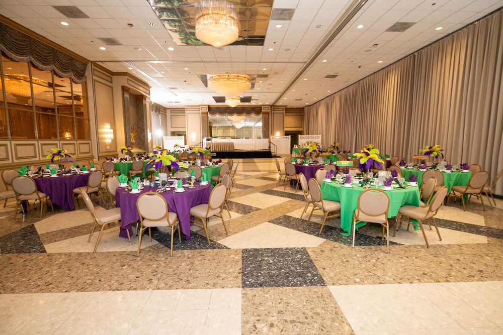 Elegant banquet hall setup with round tables decorated in vibrant purple and green tablecloths under crystal chandeliers.