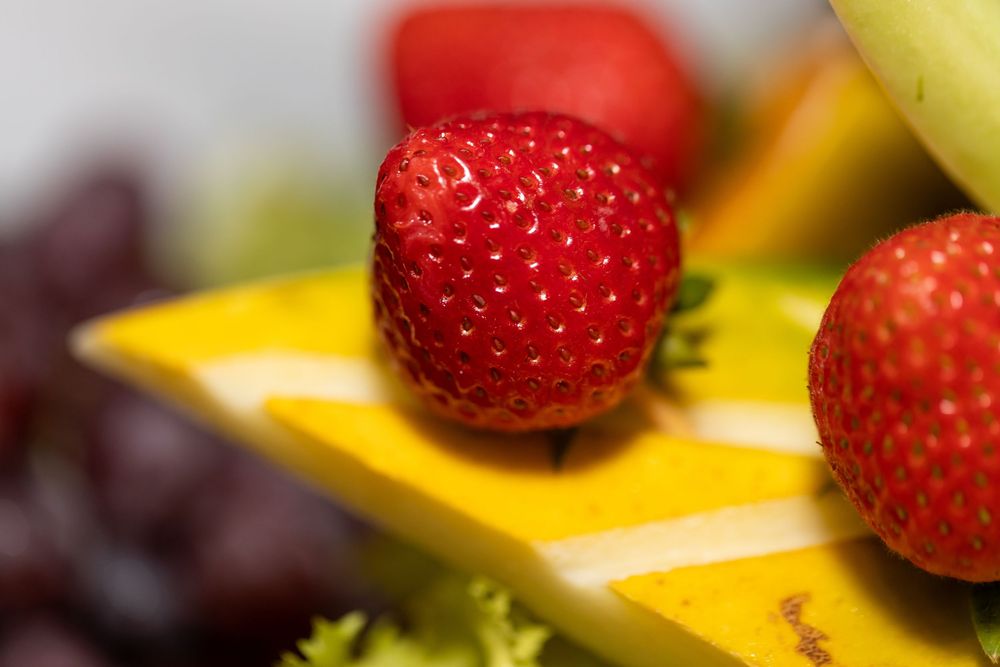 Colorful dessert platter featuring fresh strawberries and yellow custard squares arranged in rows.