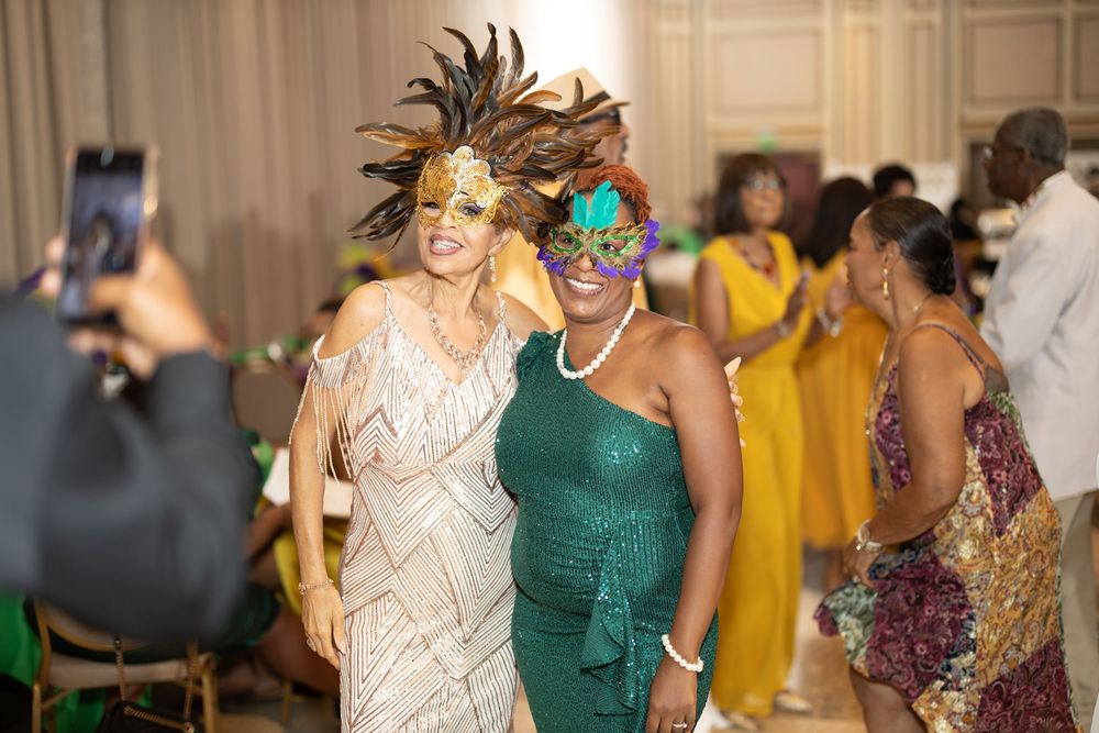 Guests in formal attire enjoying a masquerade celebration with feathered masks.
