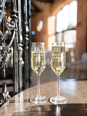 Two elegant champagne flutes filled with sparkling wine sit on a marble counter next to ornate iron decor.