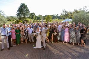 Large group of wedding guests gathered outdoors for a panoramic photo on a sunny day at an elegant venue.