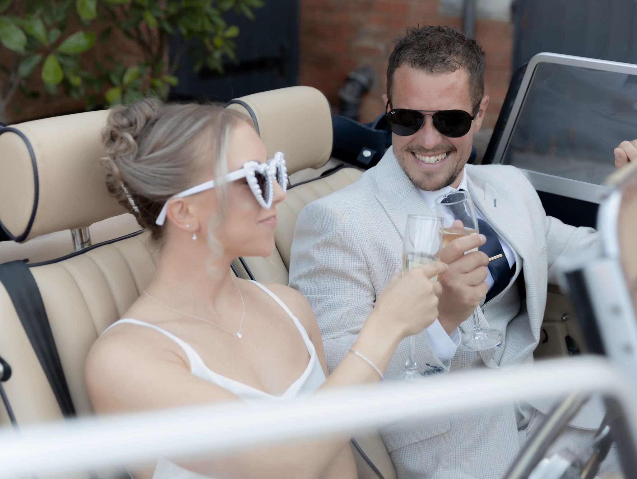 Guests seated at an outdoor wedding reception with white decor and natural greenery in the background.