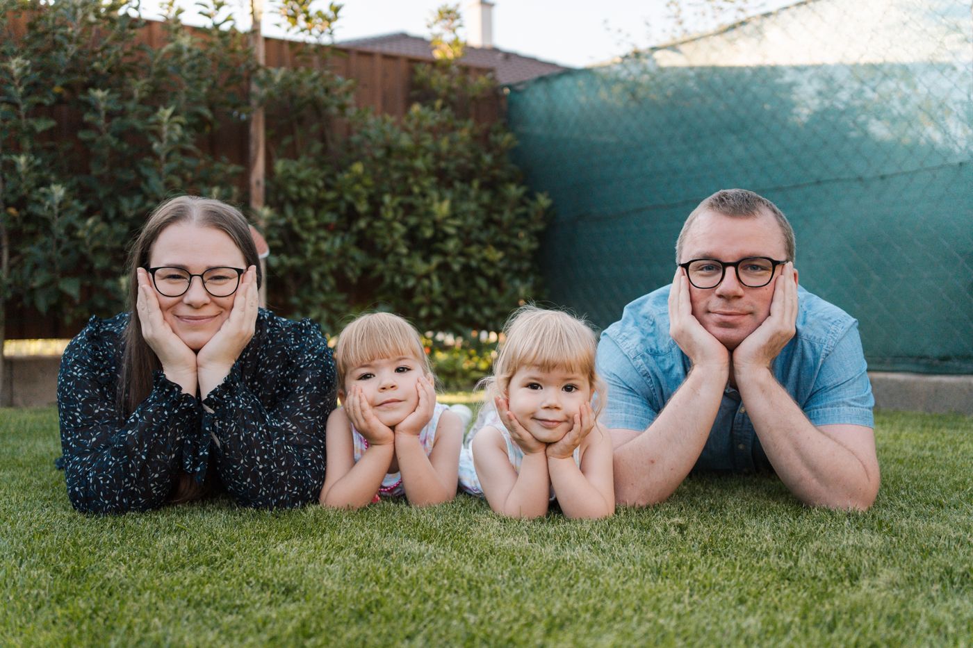 Family members lying on grass in a row with heads propped up on hands for outdoor portrait session in Rouse hill Sydney