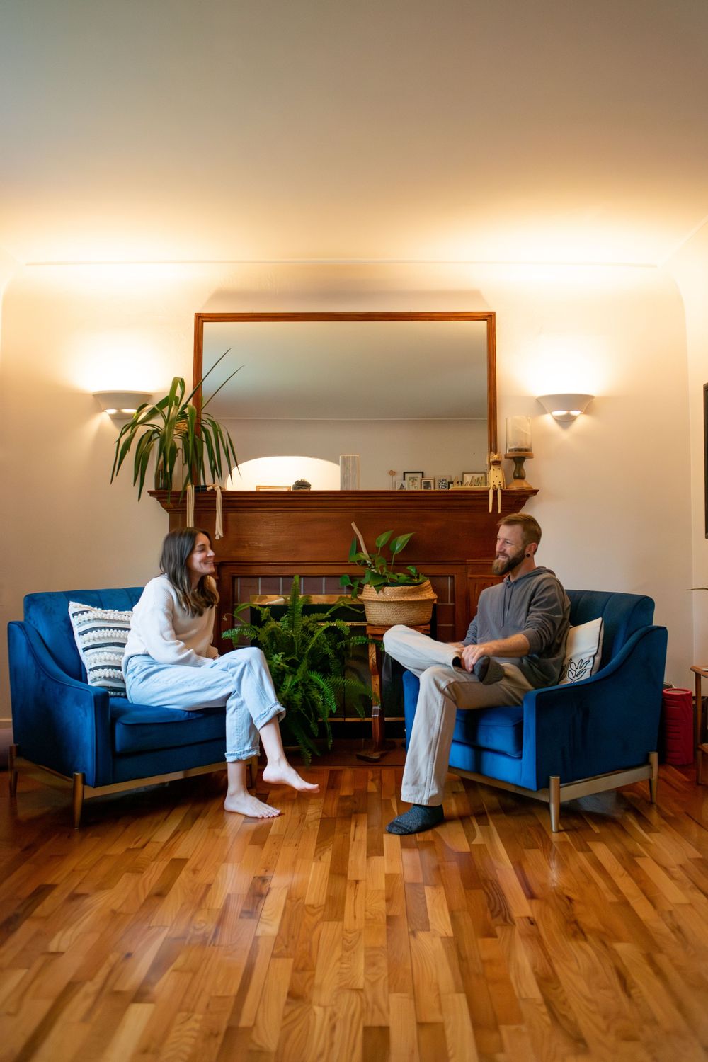 A couple sitting across from each other, with coffee, in blue chairs in their living room in Lansing, Michigan
