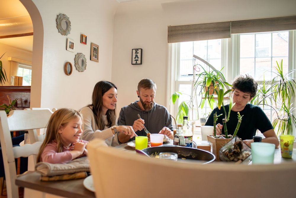 A mom and dad, oldest son, and middle daughter eating brunch together at the family dining room table in their home in Lansing, Michigan