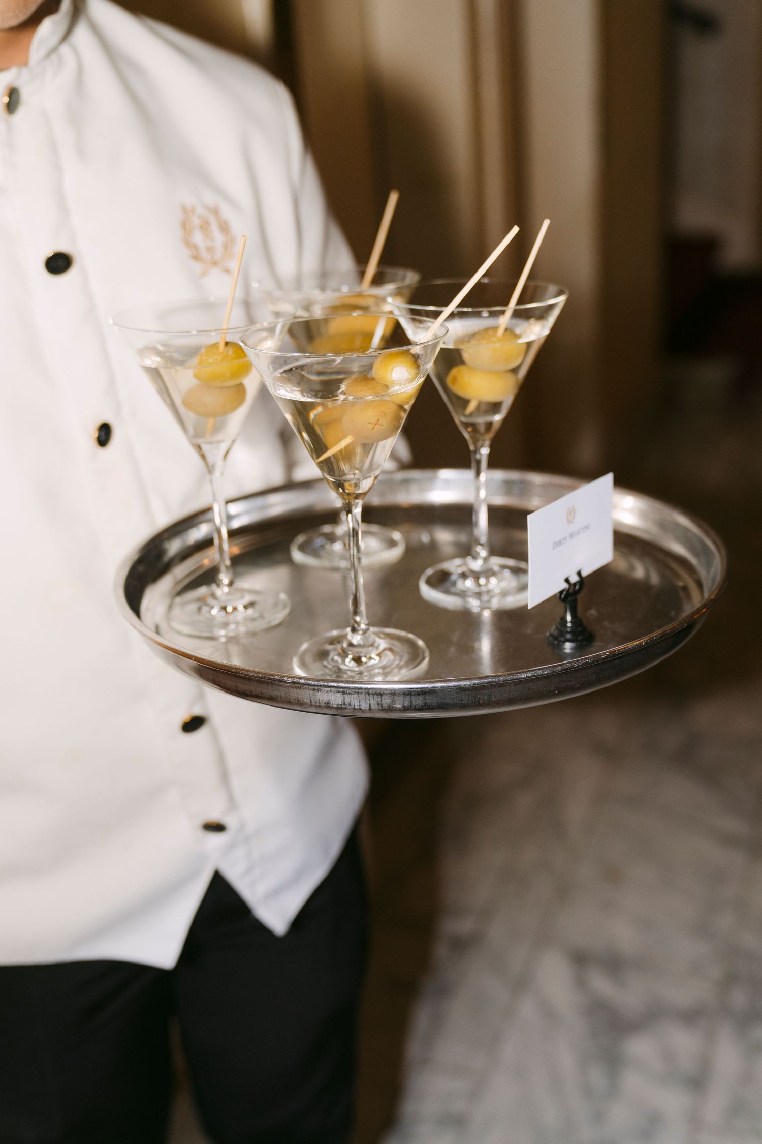 A silver serving tray holds elegant martini glasses garnished with citrus slices at an upscale event.
