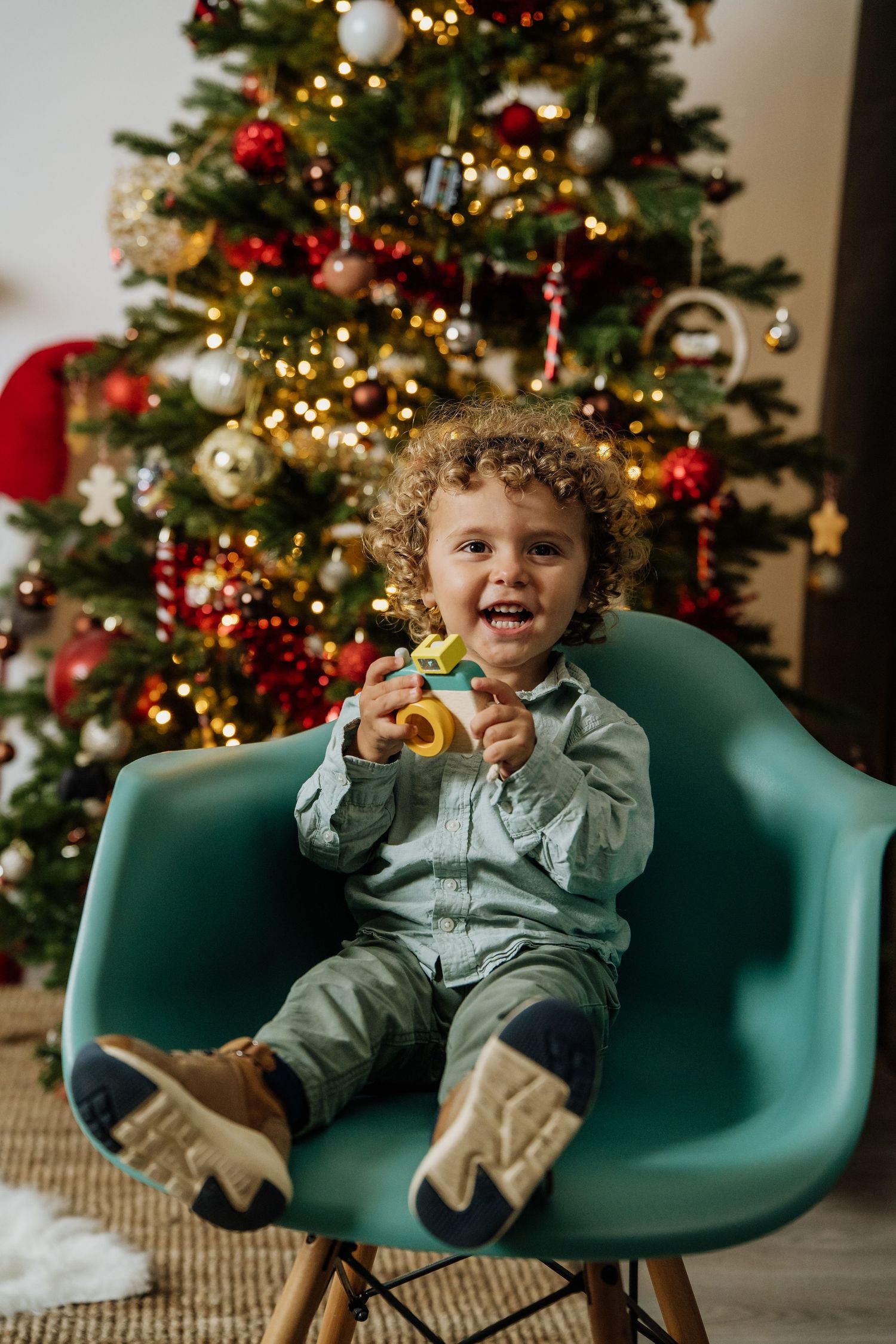 A sequence of three photos showing a child sitting in a teal mid-century modern chair by a decorated Christmas tree.