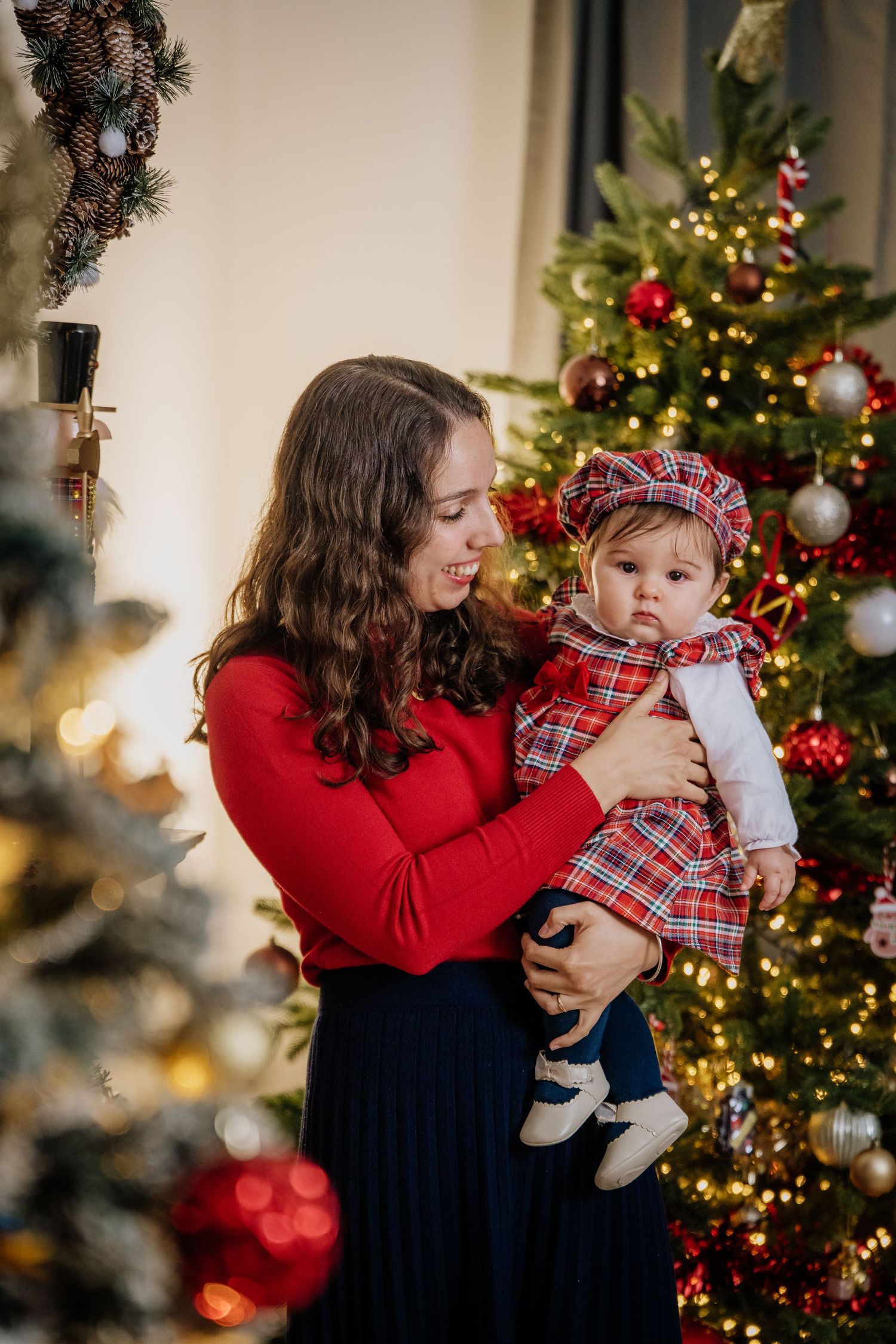 A parent and child share joyful moments in front of a decorated Christmas tree with twinkling lights and ornaments.