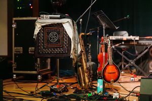 Musical instruments and equipment including mandolin, guitar pedals, and amplifiers set up on a dark stage during a live performance.