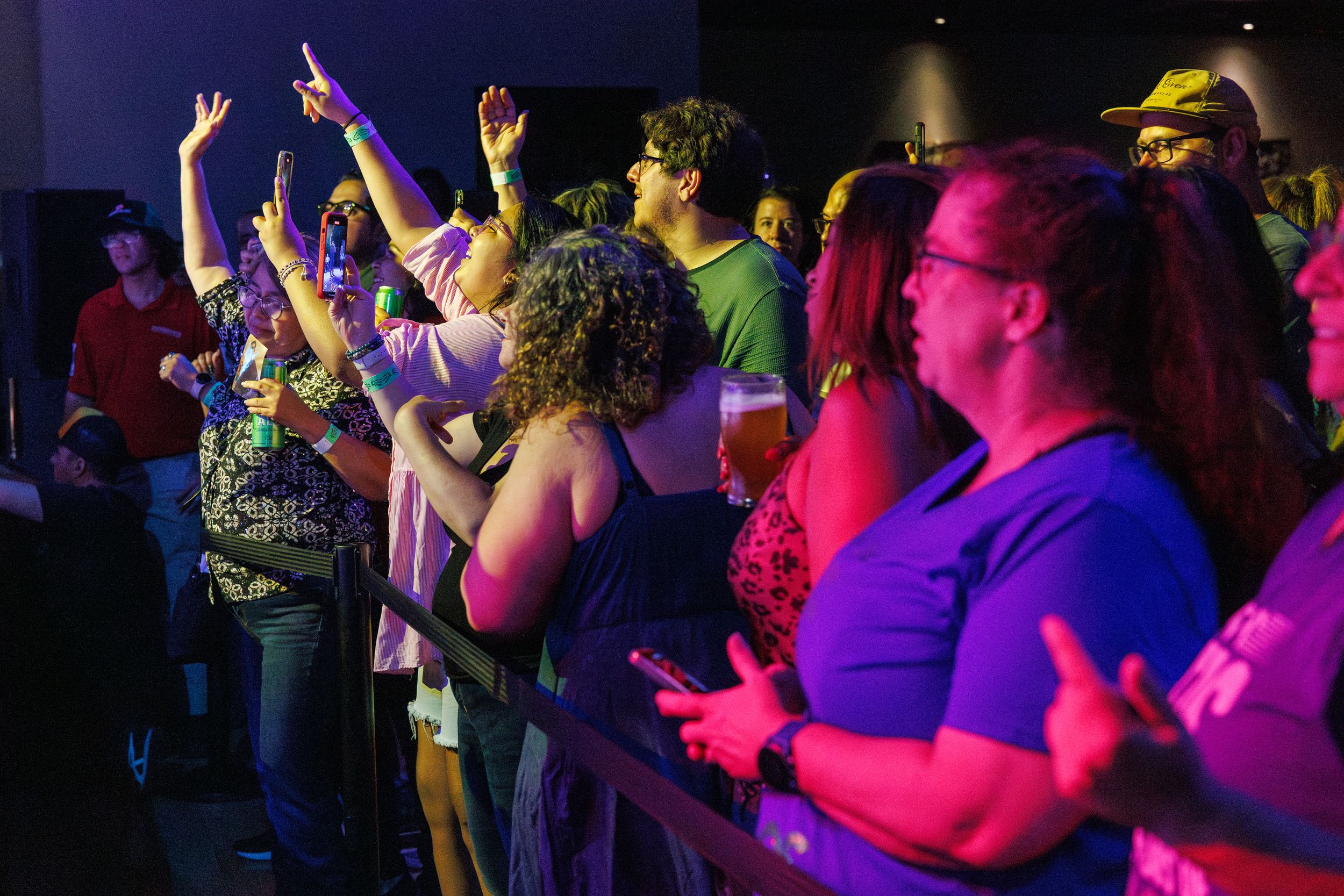 Concert audience members raising their hands and singing along during a live music performance in a dark venue.
