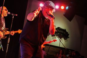 A band performs on stage under dramatic red lighting during a live concert performance.