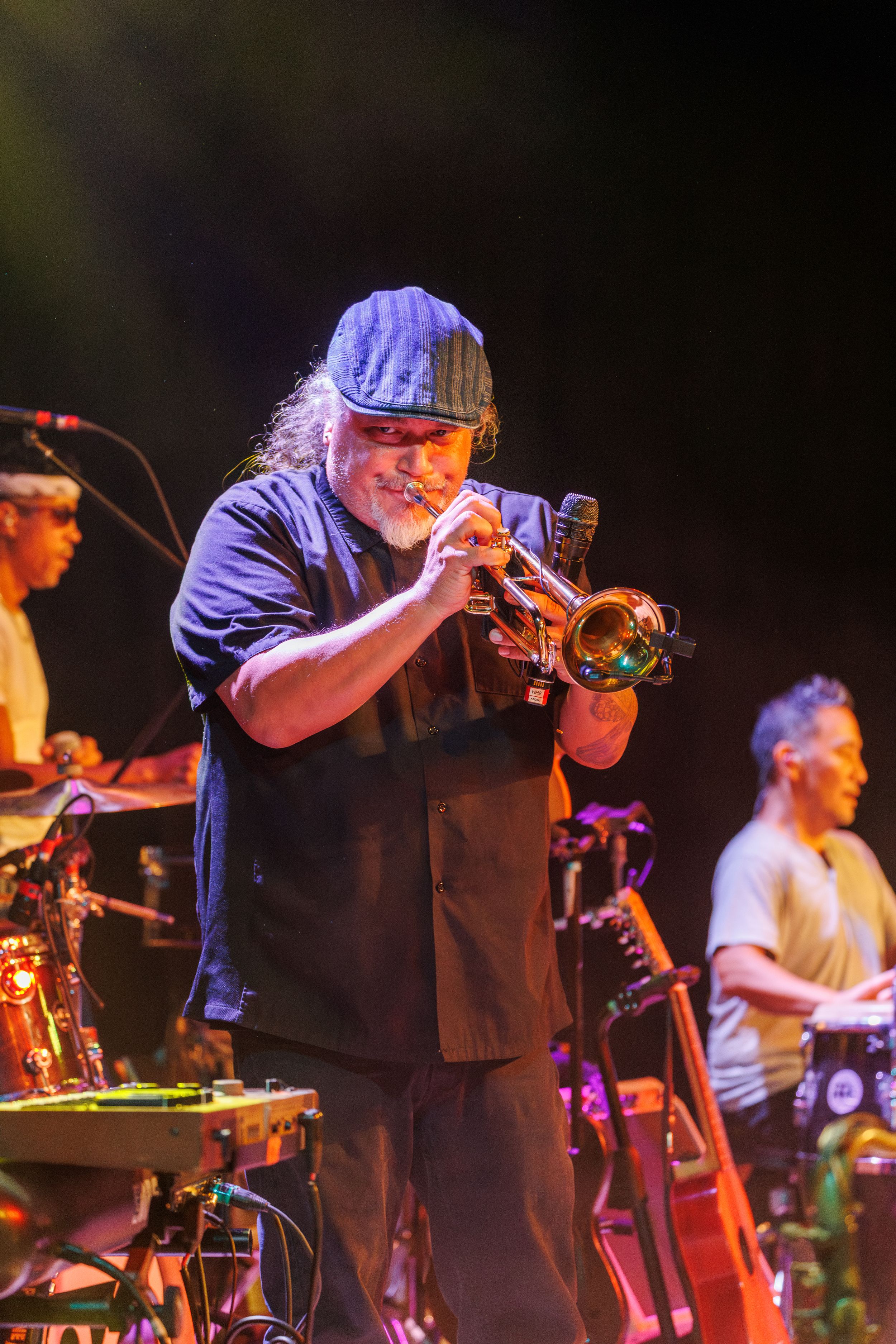 Musicians perform on stage with trumpet player and band members during a dynamic nighttime concert performance.