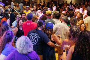 Large crowd of people dancing and enjoying music at a vibrant indoor event with colorful lighting.