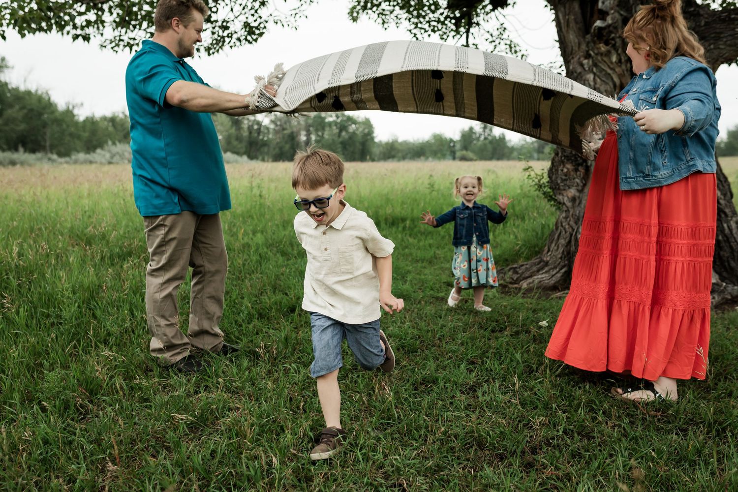 Kids playing with a blanket for summer family photos at Fish Creek Park in Calgary by lifestyle photographer Love & Sunshine Photography.