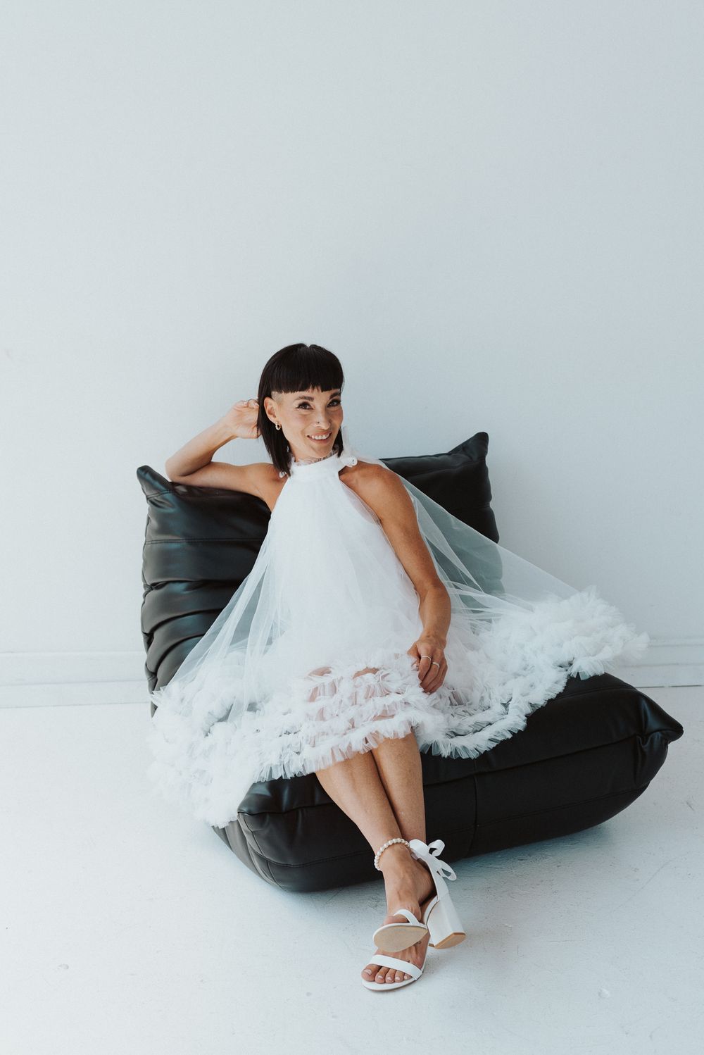 Flowing white lace dress draped over dark cushion in minimalist setting.