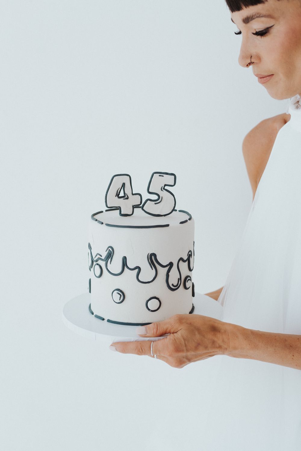 Hands holding simple white birthday cake with number 45 drawn in black.