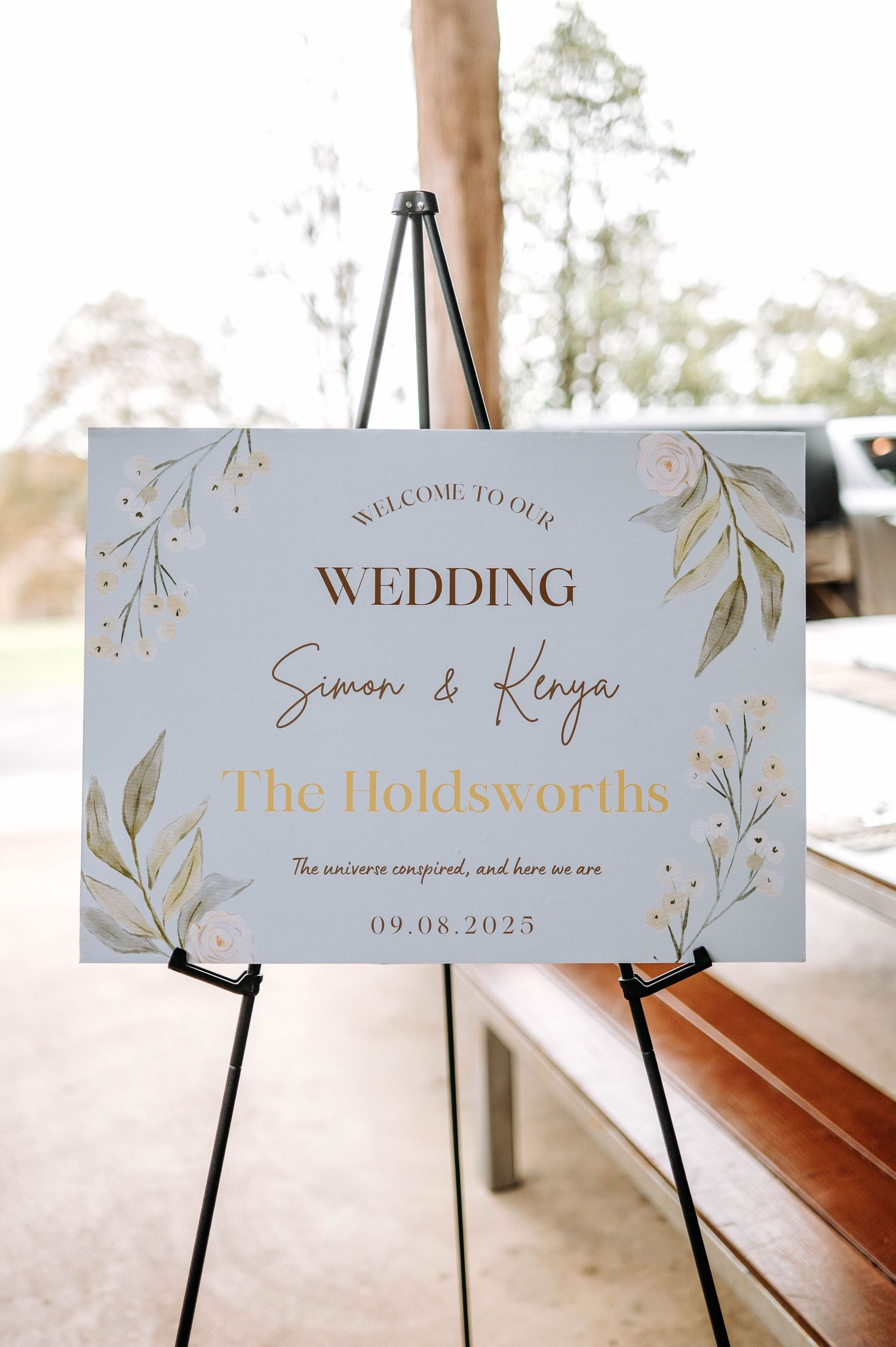 Elegant wedding reception signage displays 'The Holdsworths' and other text in gold lettering on light blue backgrounds.