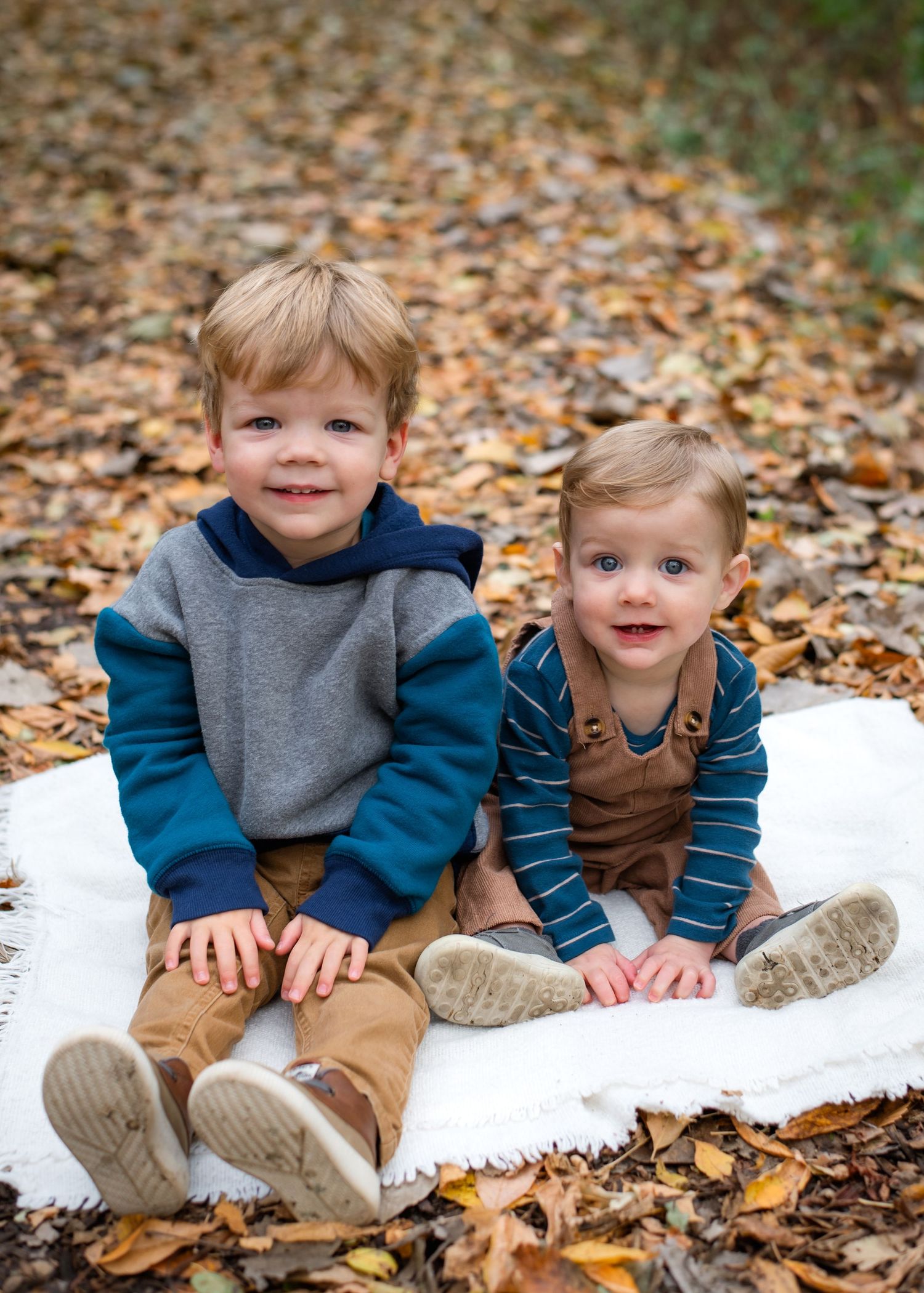 Two children playing together in fallen autumn leaves on a woodland path during fall season.