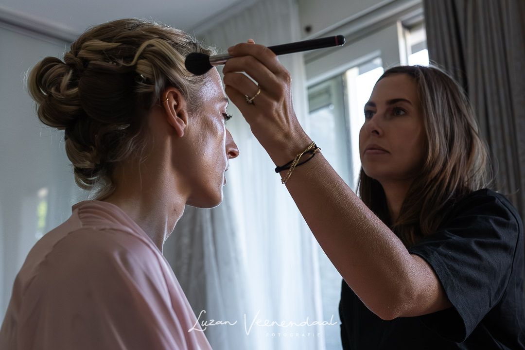 De bruid zit thuis en laat zich in de make-up zetten door de make up artist. poeder op de huis tegen het glimmen, de spanning stijgt