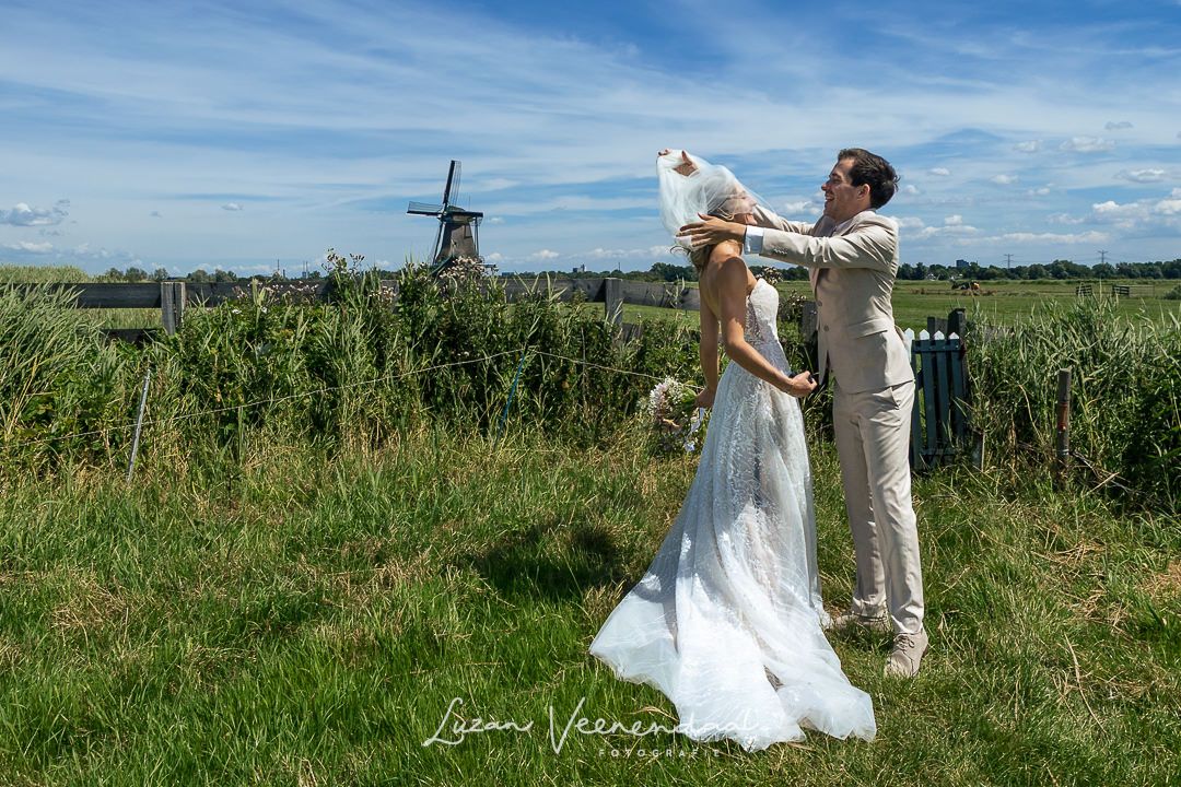 Lopend over het pad naar de molen waait de sluier van de bruid over haar hooft. De bruidegom probeert de sluier weer goed te doen.