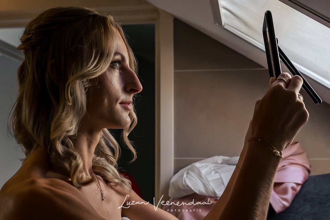 In de badkamer kijkt de bruid nog even in de spiegel of de haren en de make-up goed zitten. Er valt mooi licht door het dakraam nar binnen.