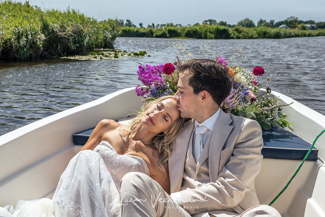 Het bruidspaar gaat per boot naar de trouwlocatie in Westzaan. Ze varen tussen de weilanden. De bruid legt haar hoofd tegen zijn schouder
