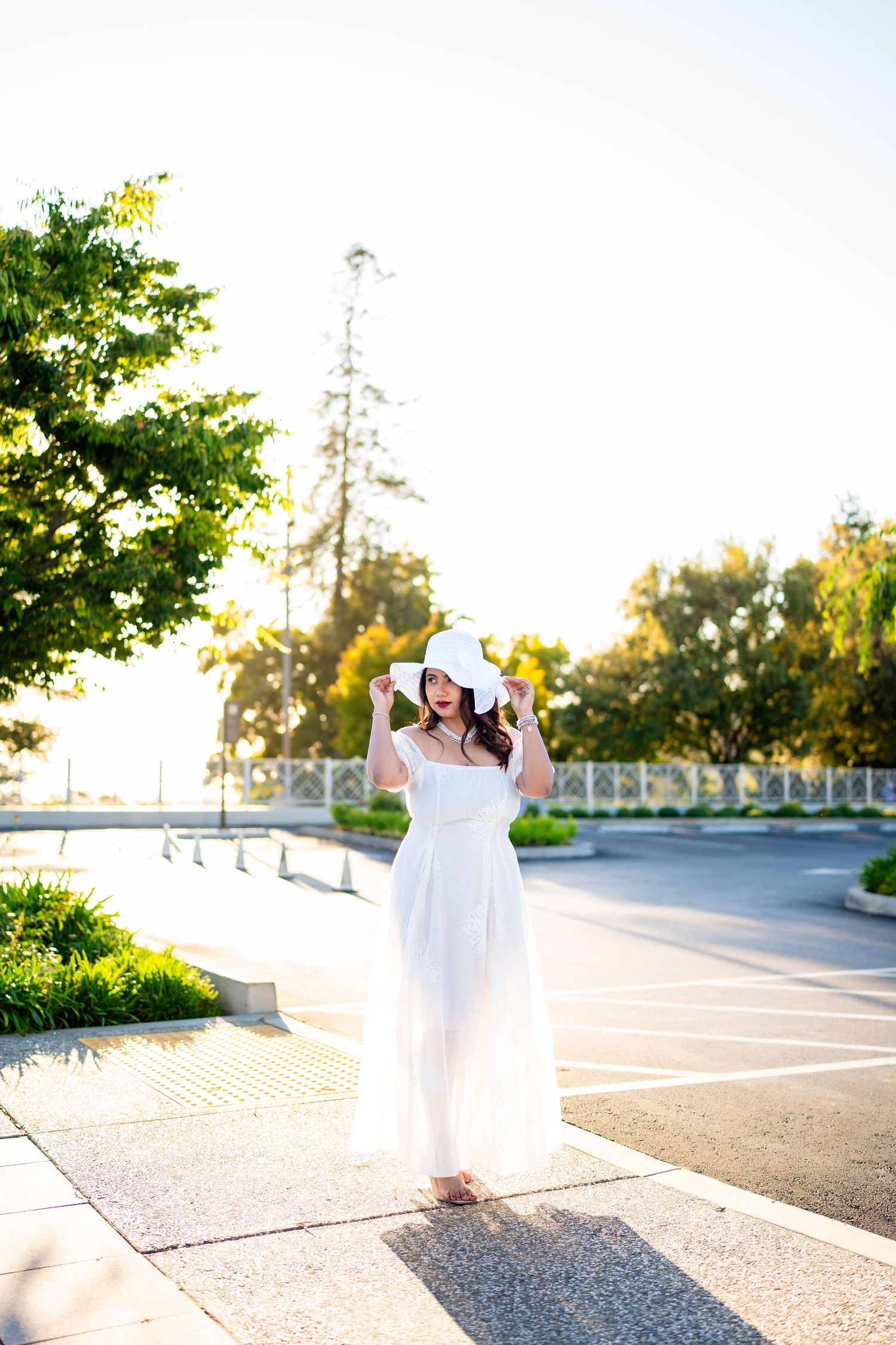 Four images of someone in a flowing white dress twirling and dancing in an outdoor parking lot at sunset.
