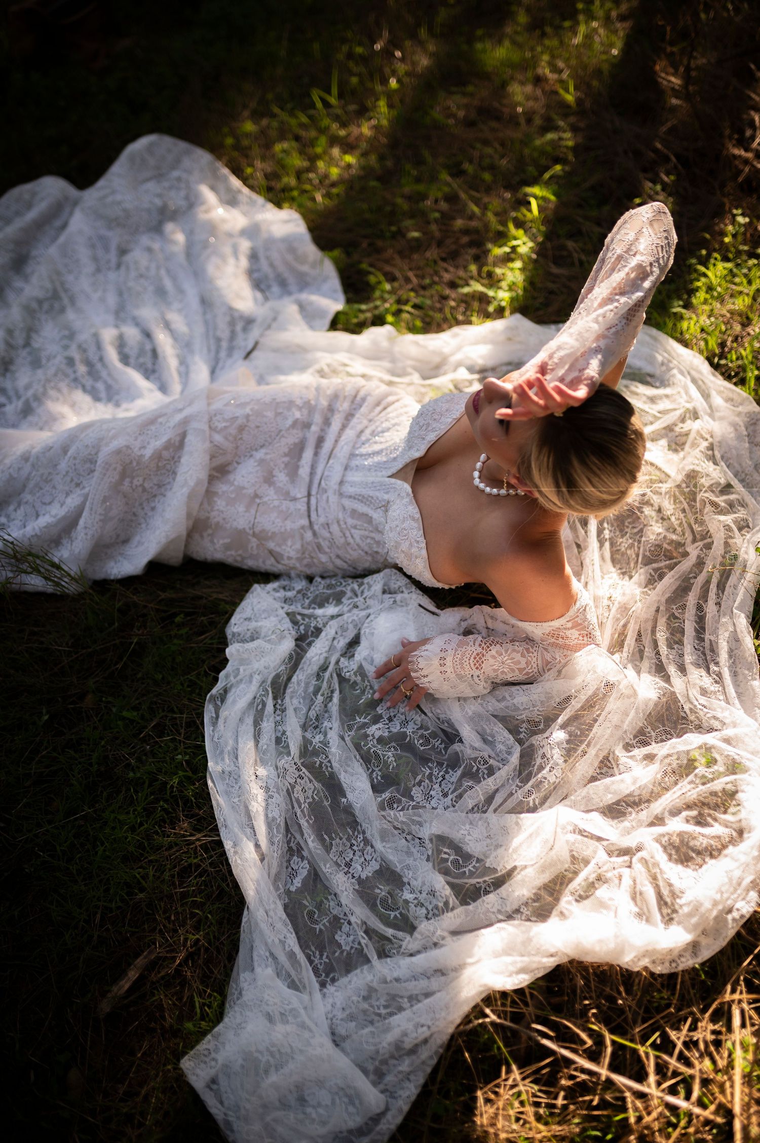 A delicate white lace wedding dress flows across sunlit grass in an artistic outdoor photography series.