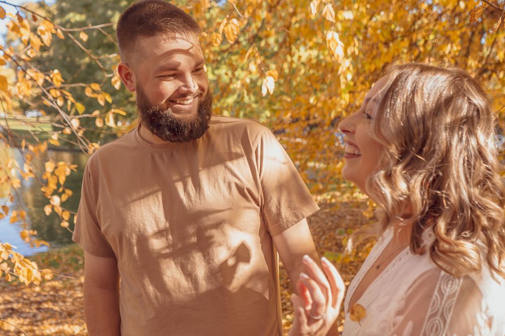 A couple shares a romantic moment outdoors surrounded by golden autumn leaves and sunlight filtering through trees.