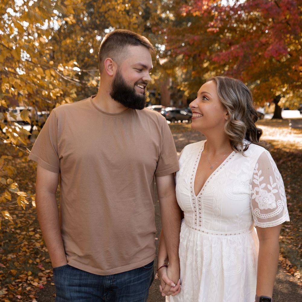 A couple walks together amidst vibrant autumn foliage in a romantic outdoor photoshoot session.