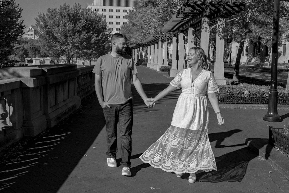 A couple holds hands while walking along a romantic riverfront promenade in black and white.