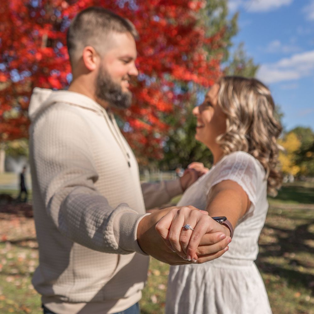 A romantic couple embraces under vibrant red fall foliage on a sunny autumn day during a photoshoot.