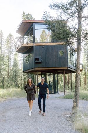 A modern cabin nestled among pine trees with a couple walking nearby.