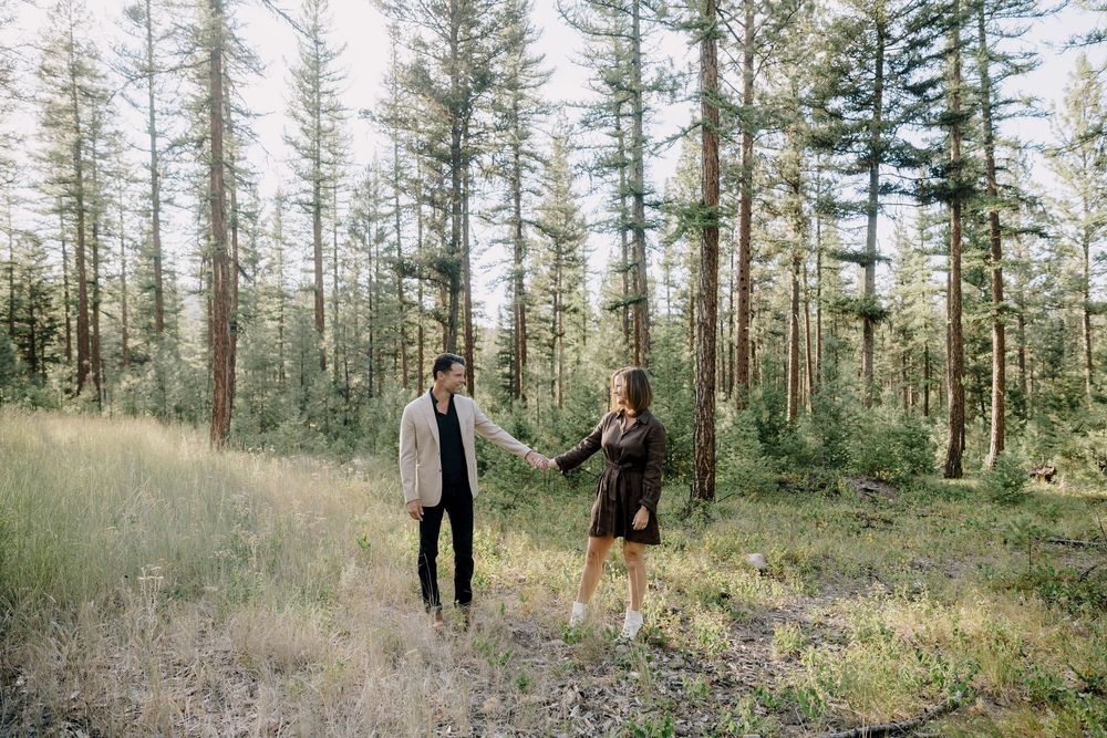 A couple walks hand in hand through a serene forest landscape.